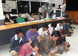 Nine drug suspects sit on the floor in front of the three suspects with the added charge of attempted bribery.